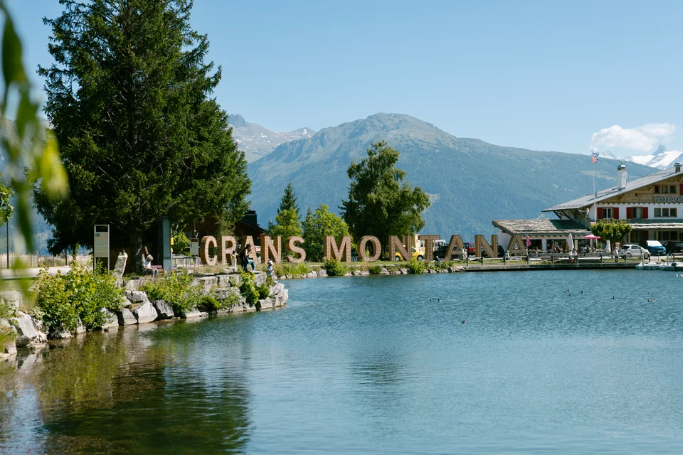 Il lago, le montagne e la scritta Crans-Montana in estate.